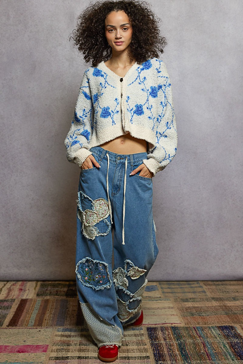 Woman wearing a floral hoodie and patchwork jeans standing against a plain background