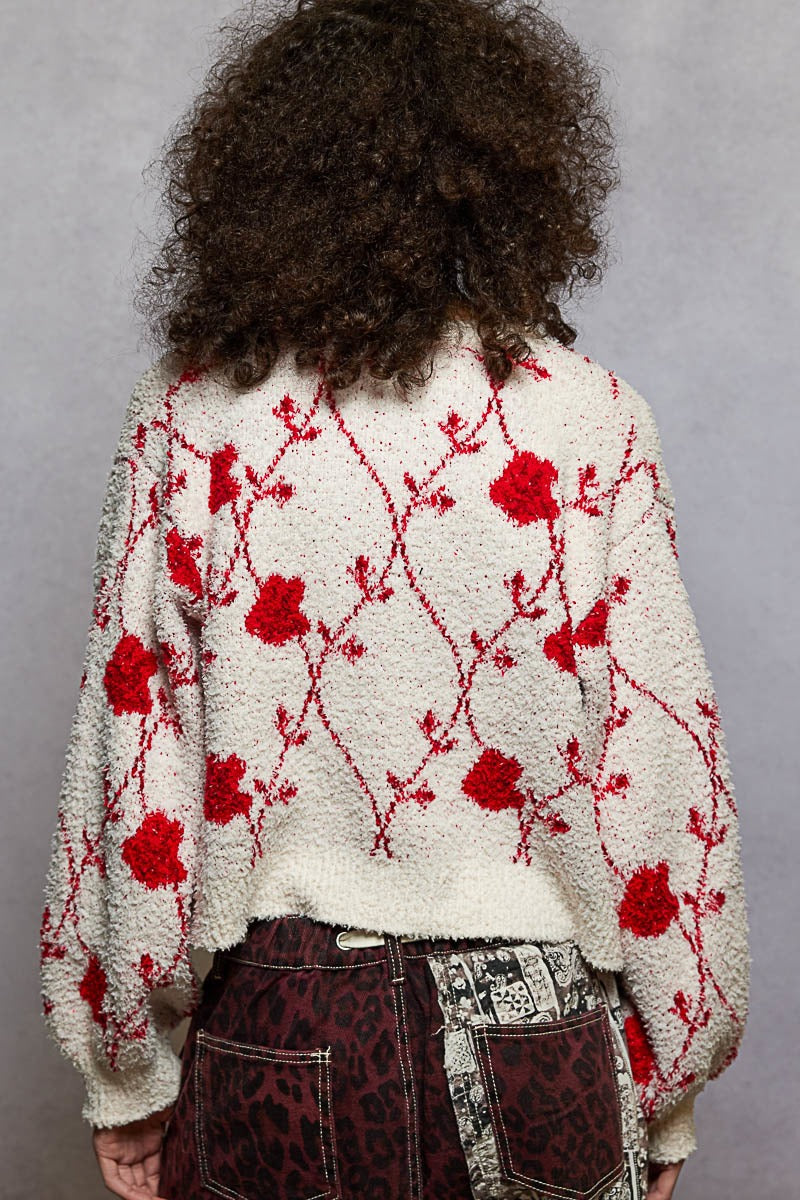 Person wearing a white sweater with red floral patterns against a gray background