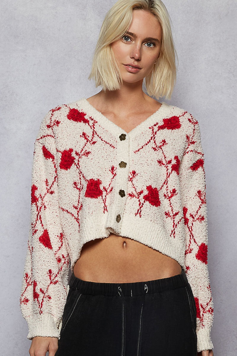 Woman wearing a white cardigan with red floral patterns against a gray background