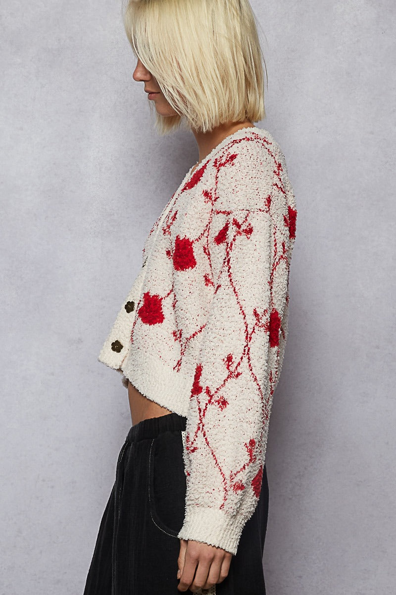 Person wearing a white cardigan with red floral patterns against a plain background