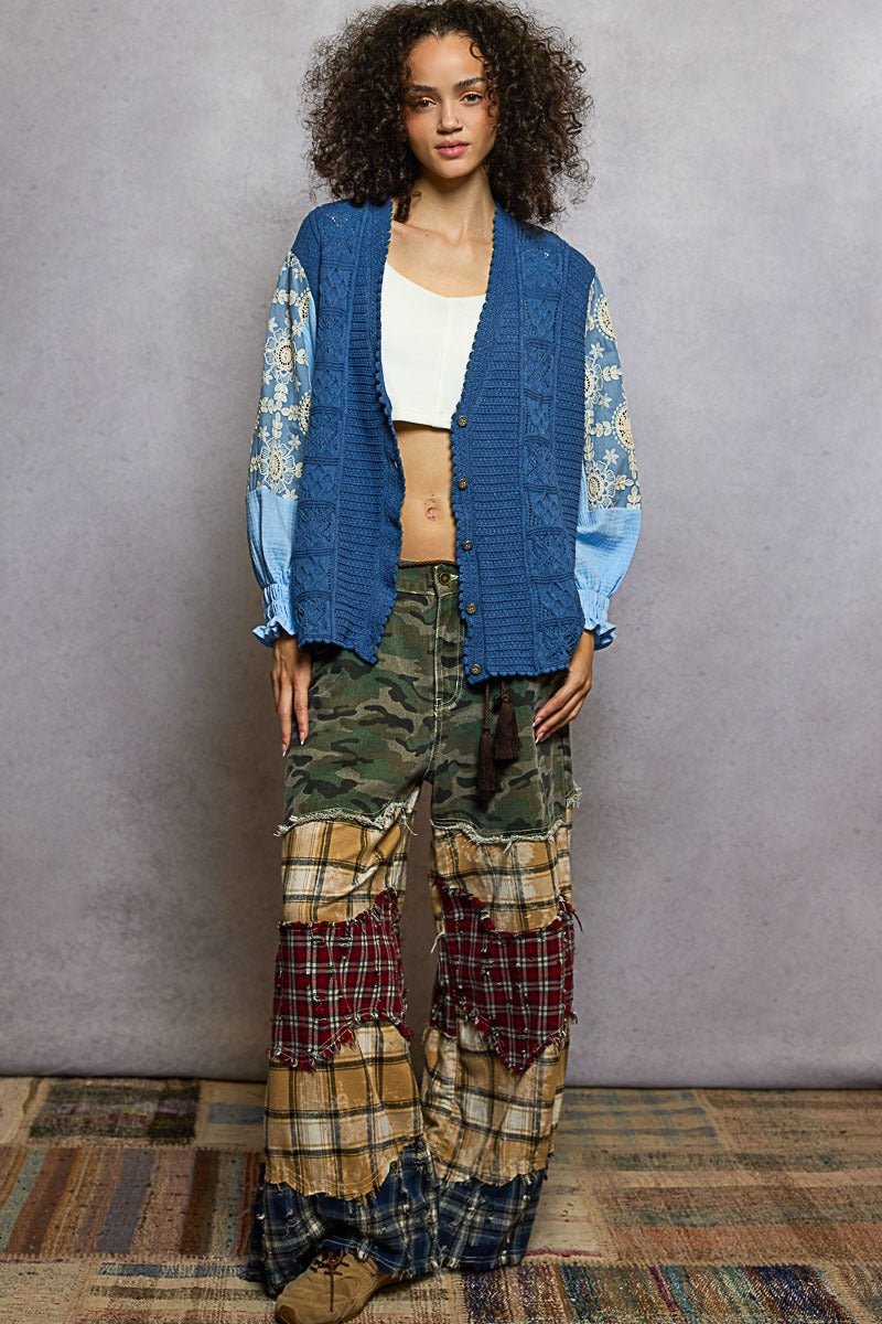 Person wearing a blue cardigan with floral patterns, white top, and plaid pants against a gray background.