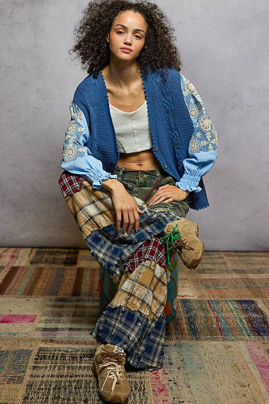 Person wearing a blue patterned cardigan over a plaid skirt on a textured floor.