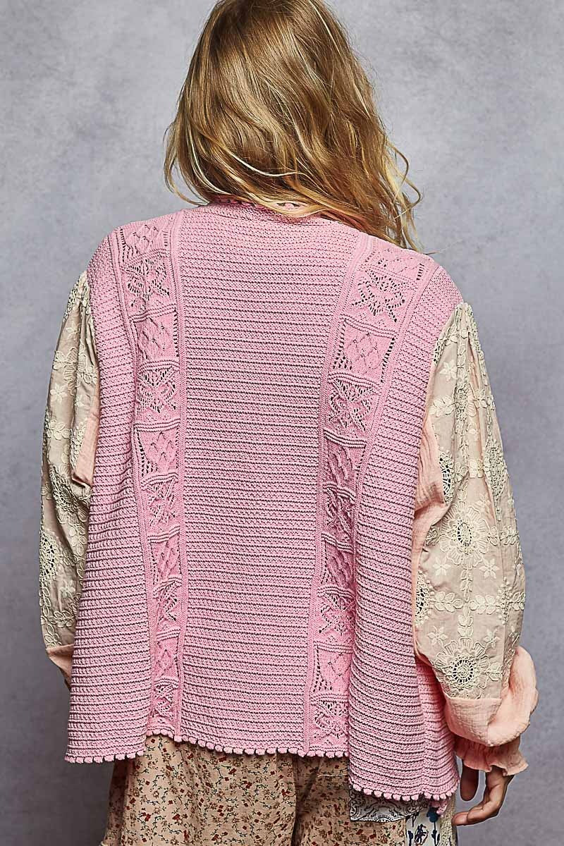 Person wearing a pink knitted vest over a patterned shirt against a gray background