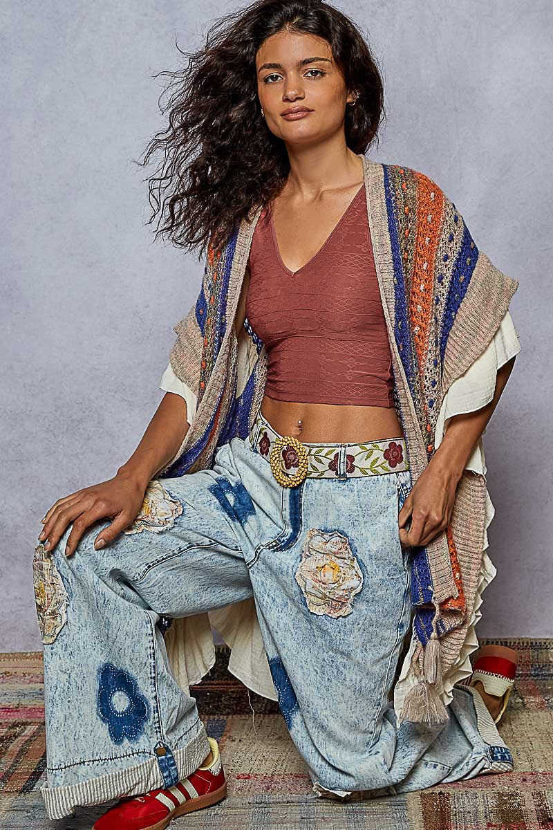 Woman wearing a colorful outfit with a patterned shawl and jeans on a textured floor.