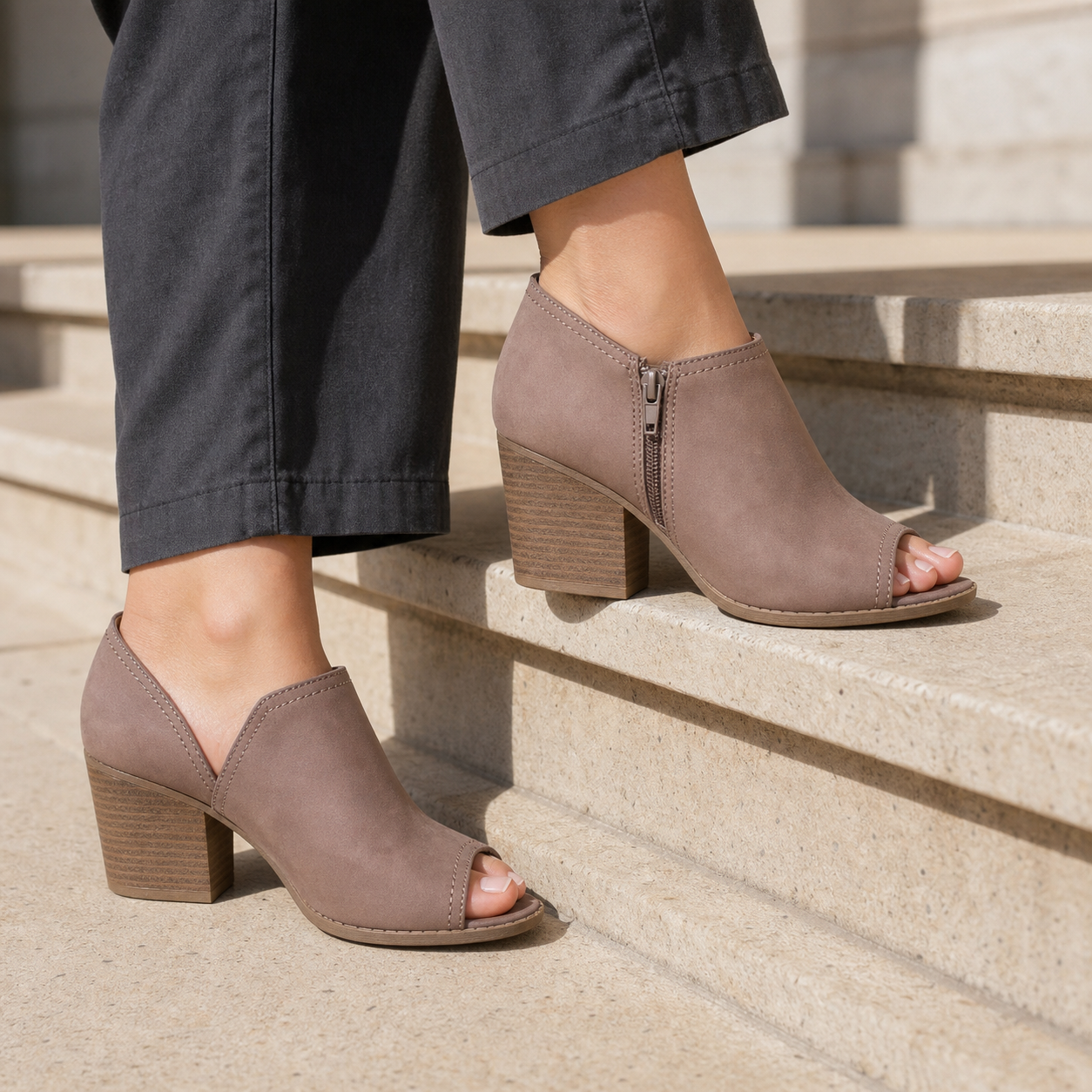 Close-up of Qupid Nutmeg peep-toe bootie on model showing center rear zip and stacked block heel on stone steps
