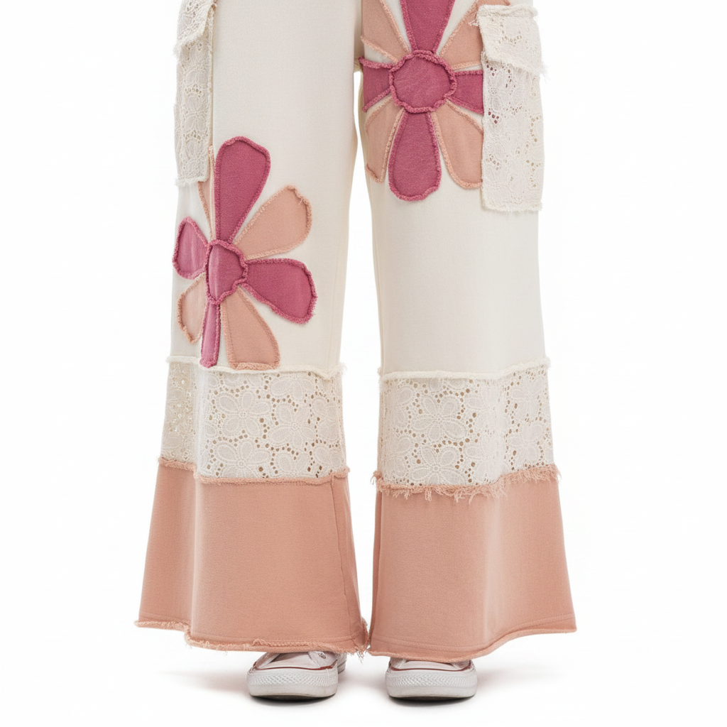Women's cream pants close-up, pink daisy appliqué detail, frayed petals, eyelet lace texture, peach color-block