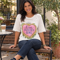 A Rare Bird Shop ivory Lion Hearted Girl tee with half sleeves past the elbow on a model seated on a cafe patio