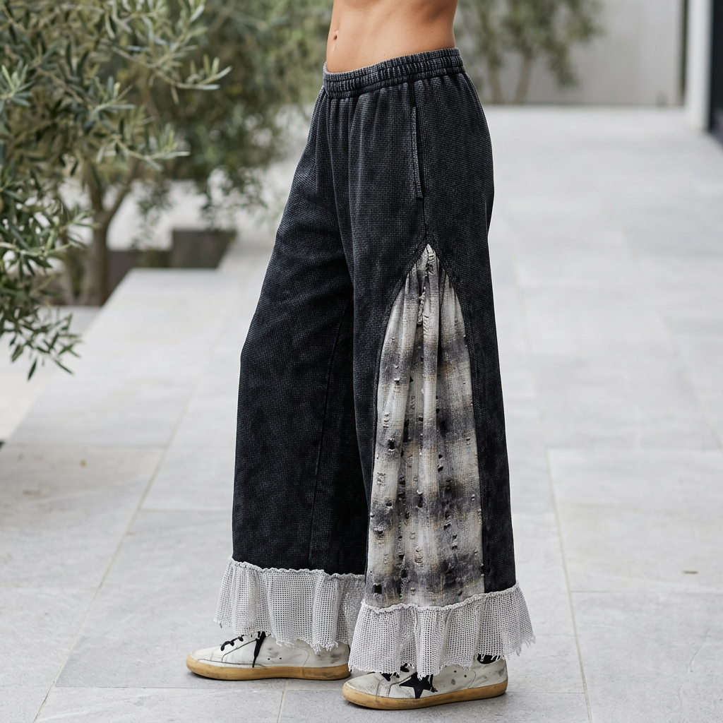 Side view of black wide-leg pants showing a distressed gray plaid panel and pale ruffle hem on a terrace.