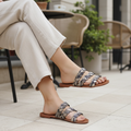 Woman seated showing outer side of Qupid Britt-11 beige brown snake-print braided slide sandals, terrace setting