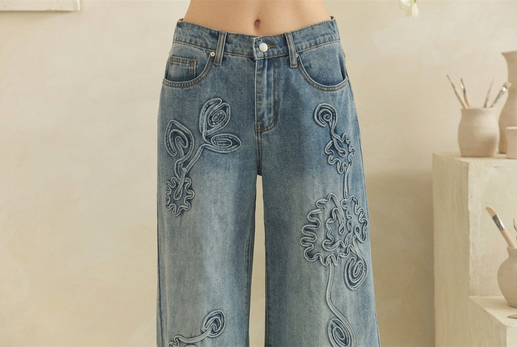 Close-up of tonal flower outlines and curling stems on the front of washed blue jeans.