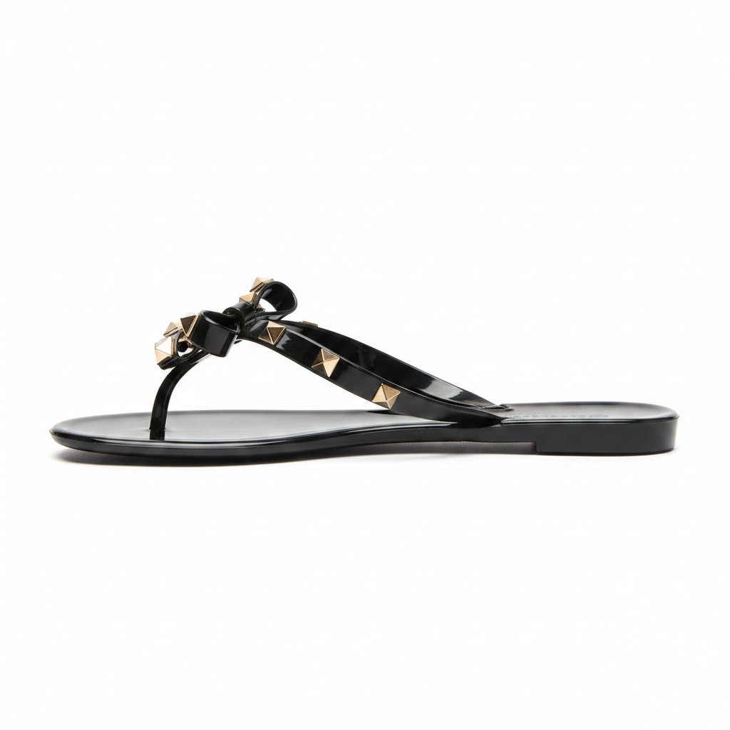 Black jelly thong sandal with gold pyramid studs and bow, side profile view showing flat sole silhouette