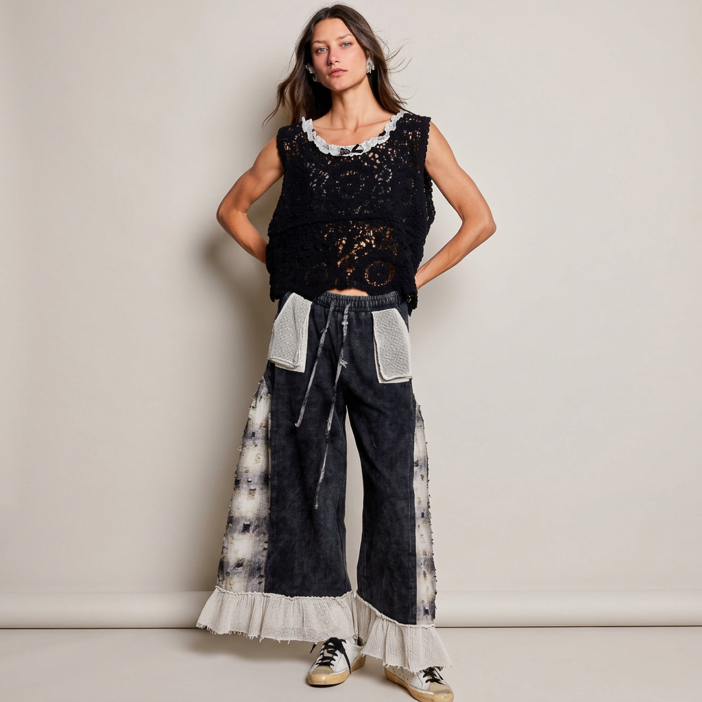 Woman in black plaid-panel ruffle pants, a black crochet top and sneakers against a light gray studio background.