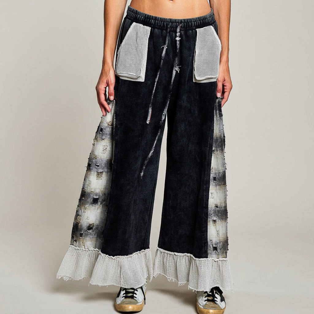 Front detail of black wide-leg pants with pale patch pockets, frayed drawstrings, plaid side panels and ruffle hems.
