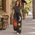 Mello women's black washed wide-leg pants with sun, moon and star appliqués, walking on a café street