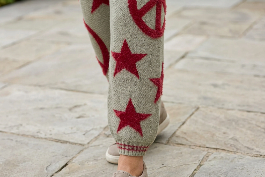 Close-up of red stars and a peace motif on olive knit joggers, finished with a red-striped cuff.