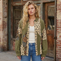 Woman wearing an olive floral patchwork gauze shirt over an ivory tank and jeans outside a brick storefront.