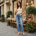 Woman in a white top and blue jeans standing on a street with cafes and plants.