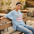 Women's light blue Americana French terry pullover top, seated café pose, open seam detail, styled with distressed jeans