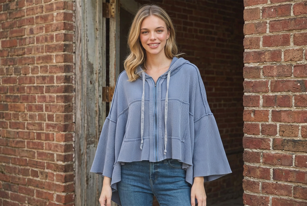 Light blue waffle zip hoodie showing the drawstring hood and wide sleeves at a brick entryway
