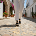 Woman wearing black espadrille platform sandals walking on Mediterranean cobblestone street, summer lifestyle