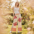 Women's cream wide-leg pants, standing, pink daisy appliqué, eyelet lace panels, peach hem, relaxed fit - BellanBlue