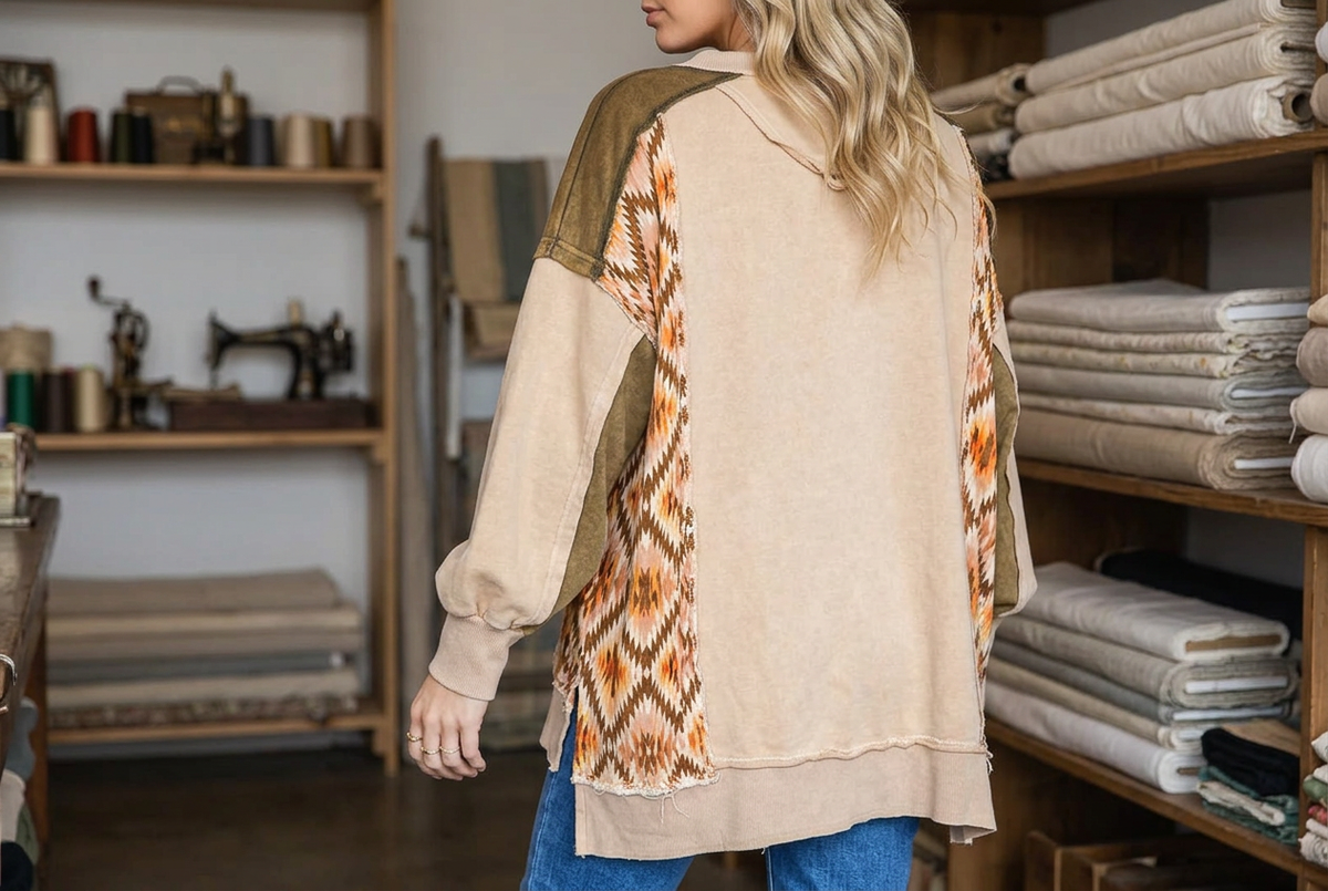 Back and side view of a tan pullover showing geometric patchwork panels and ribbed cuffs in a fabric shop