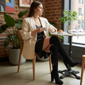Woman sitting at a cafe table holding a cup, wearing a beige blazer and black knee-high boots.