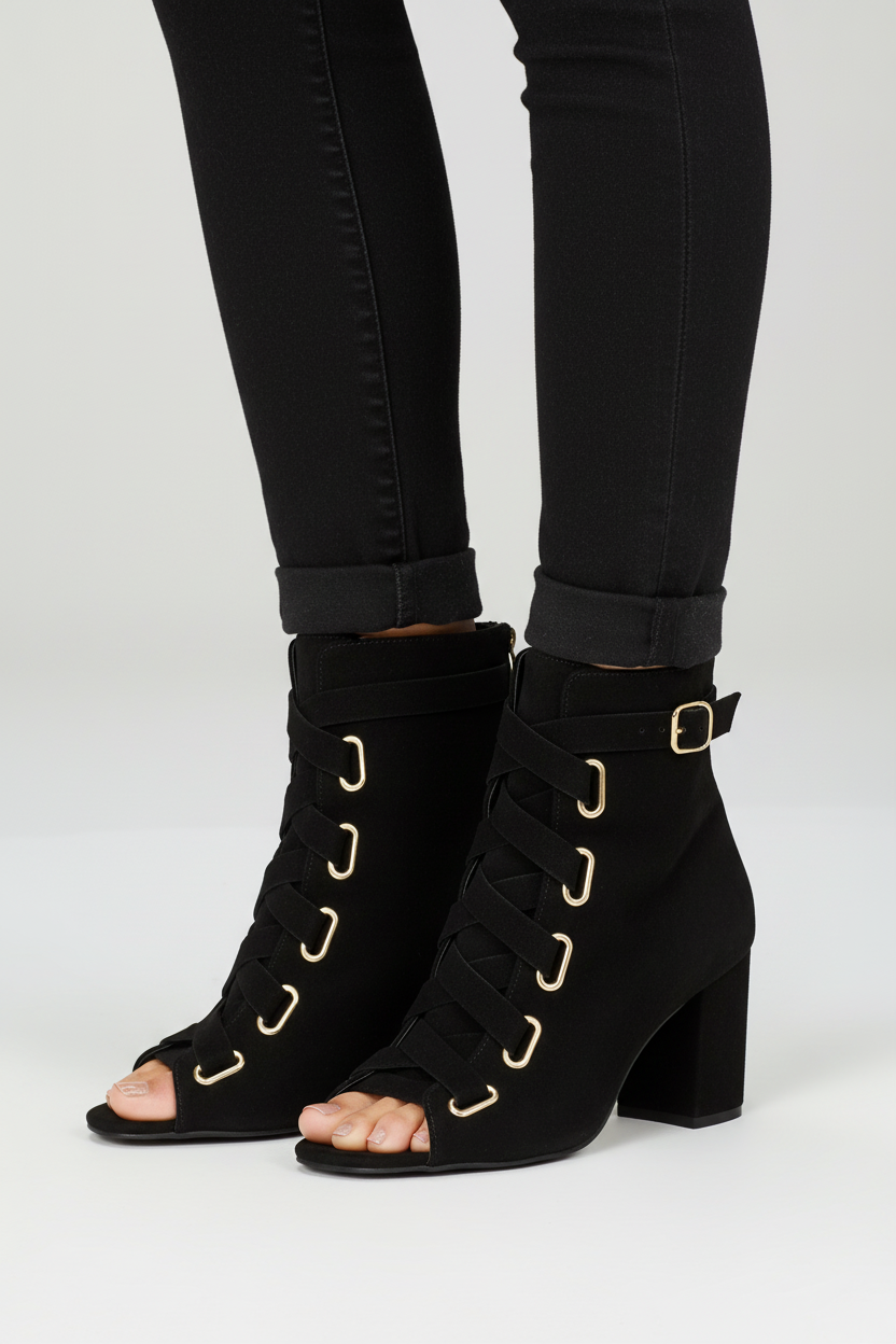 Close-up detail of black lace-up ankle booties showing metal grommets and buckle strap with skinny jeans