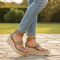 Woman wearing AMS EMMA-25 snake print espadrille wedge sandals standing outdoors, knees-down view, light wash denim