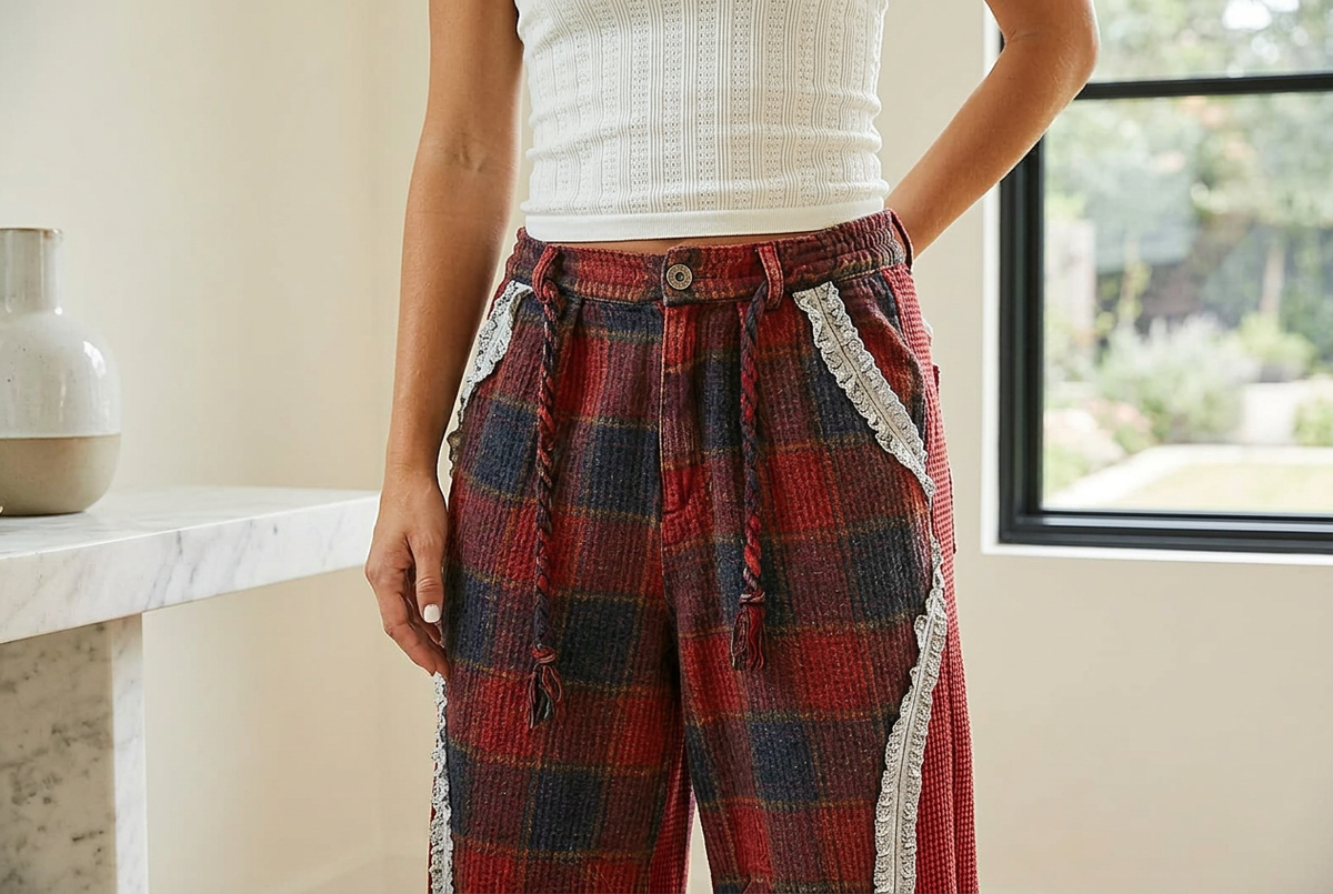 Detail of the gathered button waist and braided ties on wine plaid pants beside a white stone console