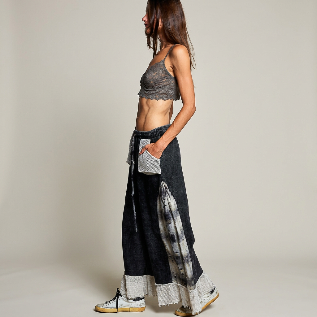 Side view of black plaid-panel ruffle pants styled with a gray lace top and sneakers against a warm-gray backdrop.