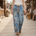 Blue star and paisley embroidered jeans styled with an ivory top and brown boots on a wooden market walkway