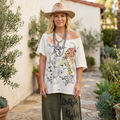 Ivory oversized off-shoulder graphic tee with sketched cat and leopard butterfly wing, worn with olive pants in a courtyard