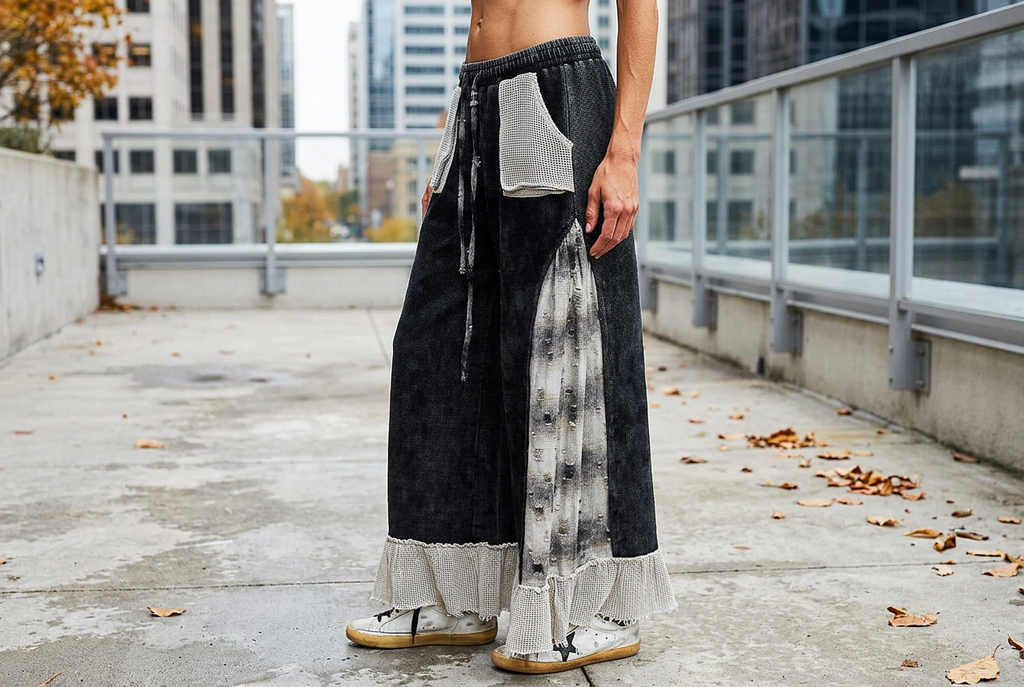 Three-quarter view of black wide-leg pants with contrasting plaid side inserts and pale ruffle hems.