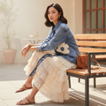 Women's Mello denim shirt dress with crochet flower detail and layered cream ruffle hem, seated styling