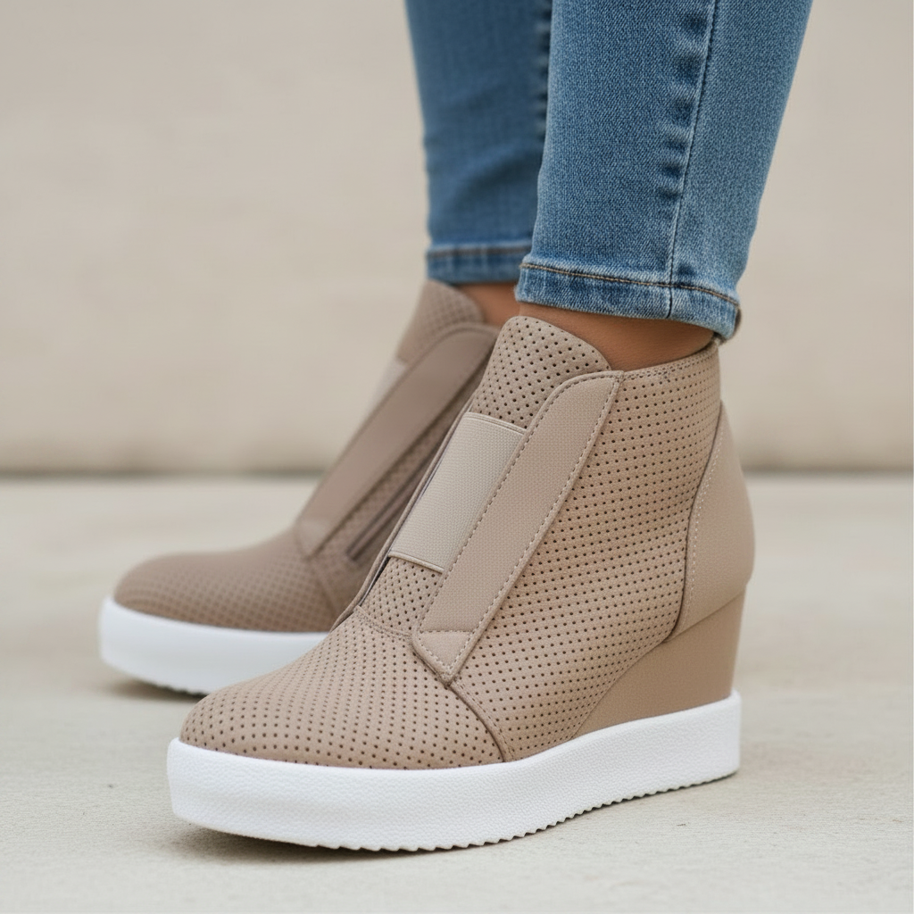 A pair of beige wedge sneakers with perforated uppers, side buckle straps, and thick white platform soles, shown on a model wearing blue jeans.