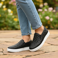 Woman on garden patio wearing black quilted slip-on platform sneakers with light wash jeans three-quarter view