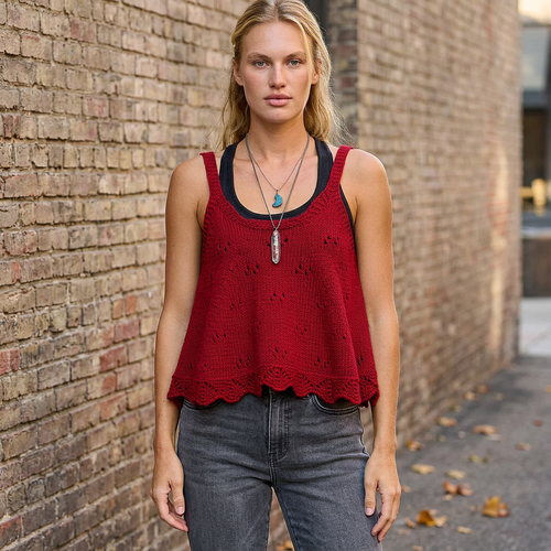 Ruby openwork knit camisole with scalloped hem over a black tank, front view beside a brick wall