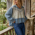 Three-quarter view of a blue and cream patchwork hoodie with a high-low hem, worn with jeans on a porch.