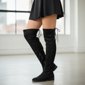 Woman standing in Verona black faux suede over-the-knee lace-up boots with mini skirt, mid-thigh down view
