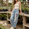 Woman leaning beside a nursery bench in blue postage print barrel jeans and cream sneakers