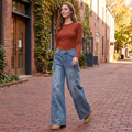 Woman walking on a brick lane in blue floral applique wide-leg jeans, a rust top and tan boots.