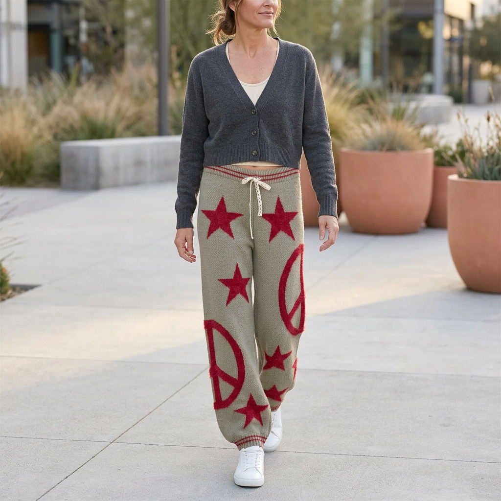 Woman walking in olive star and peace-sign knit joggers with a charcoal cardigan and white sneakers.
