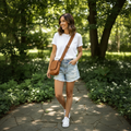 Woman walking outdoors in a park wearing a white t-shirt, denim shorts, and white sneakers.