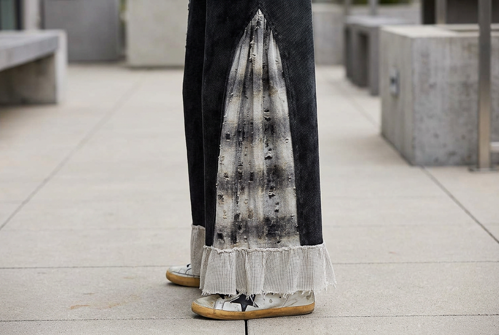 Close-up of a distressed gray plaid side panel meeting the pale textured ruffle hem of black pants.