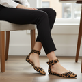 Woman seated at cafe wearing Faryl Robin leopard pointed-toe flats, outer side and bow ankle strap detail visible, ankles crossed