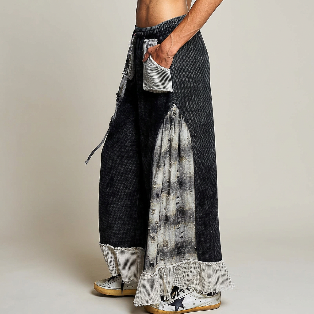 Side detail of a pale patch pocket, distressed gray plaid insert and ruffle hem on black wide-leg pants.
