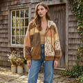 Brown floral and plaid patchwork hooded jacket worn open with jeans outside a timber cottage.