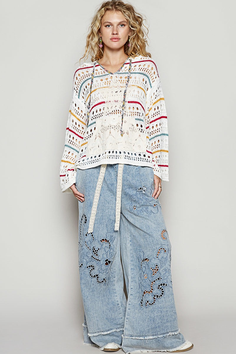 Woman wearing a colorful patterned sweater and light blue jeans on a gray background