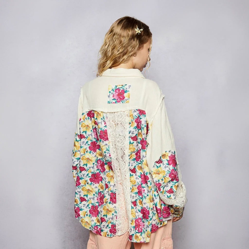 A woman shown from the back wearing a cream-colored patchwork jacket with vibrant pink, yellow, and blue floral patterns and a lace panel down the back, set against a plain gray studio background.